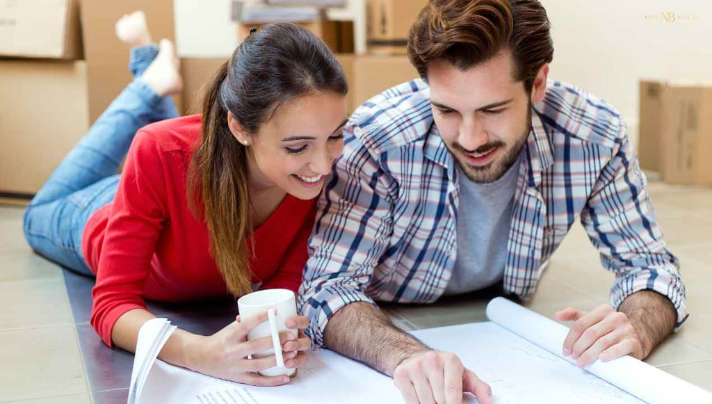 a young couple looking at building plans on the floor side by side as they choose a home builder